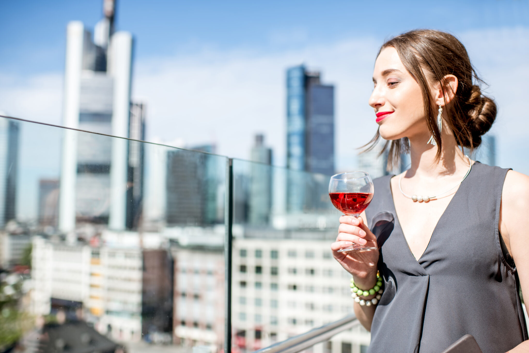 Young businesswoman enjoying wine on the terrace with great view on the skyscrapers in Frankfurt city