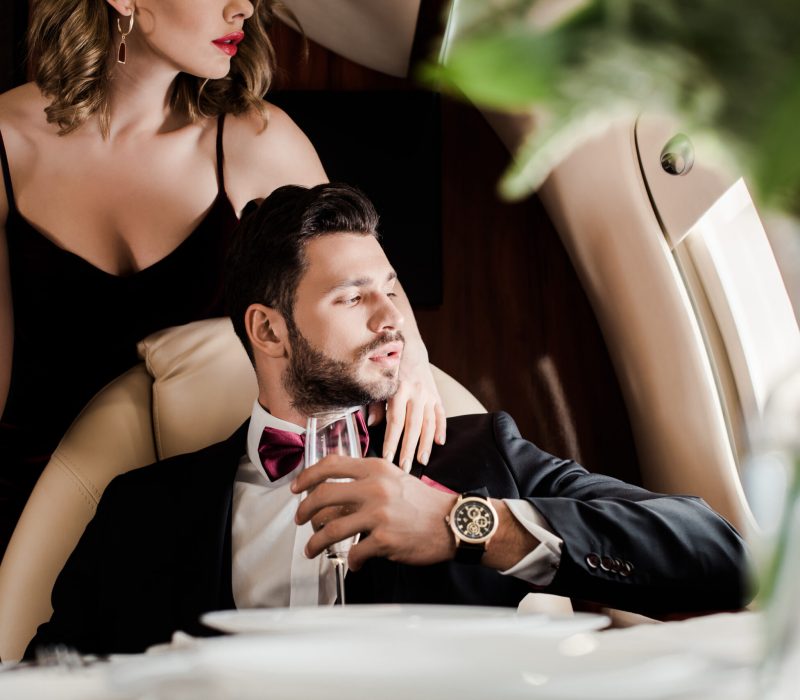 cropped view of sexy woman touching elegant man holding glass of champagne in plane